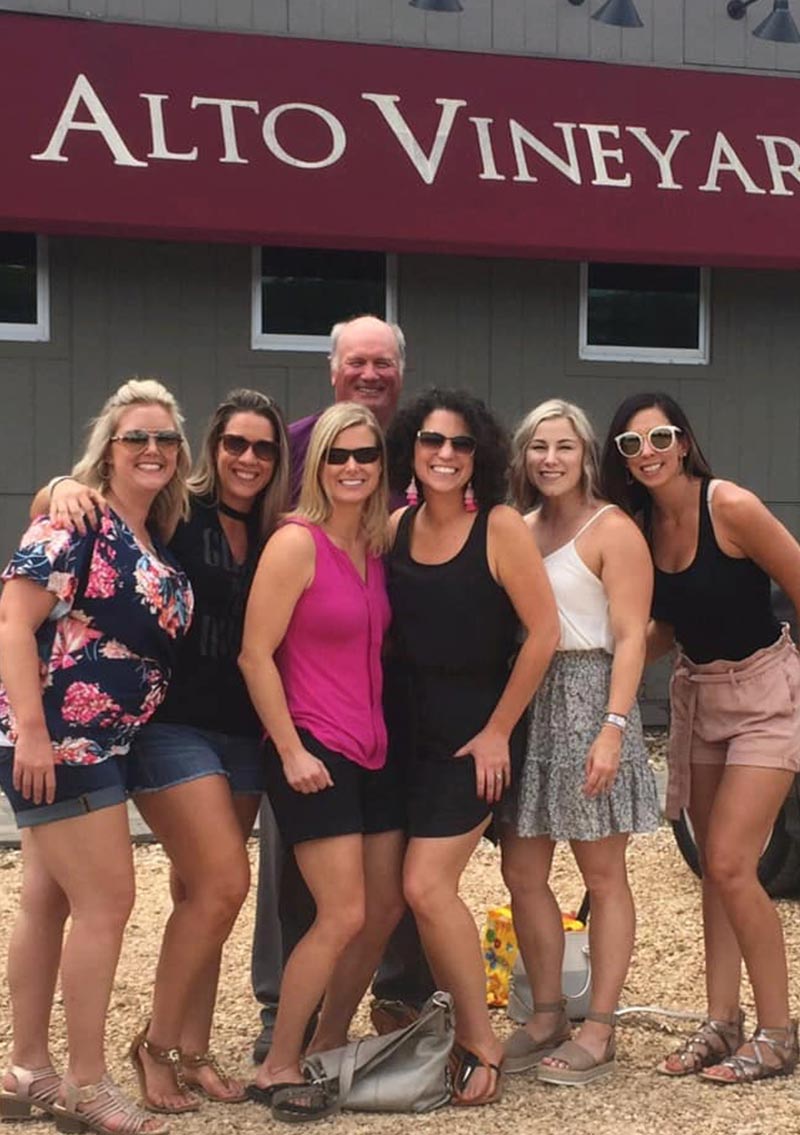 group of women and one man in front of red awning for alto vineyards