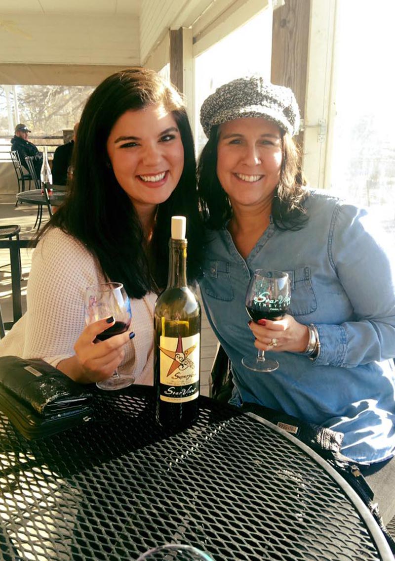 two white women smiling and enjoying a glass of red wine
