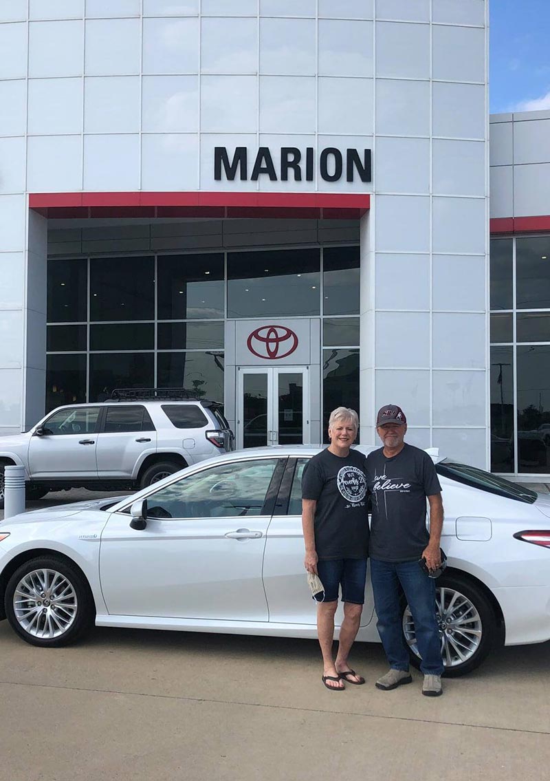exterior of toyota dealership with couple in front of their newly purchased sedan