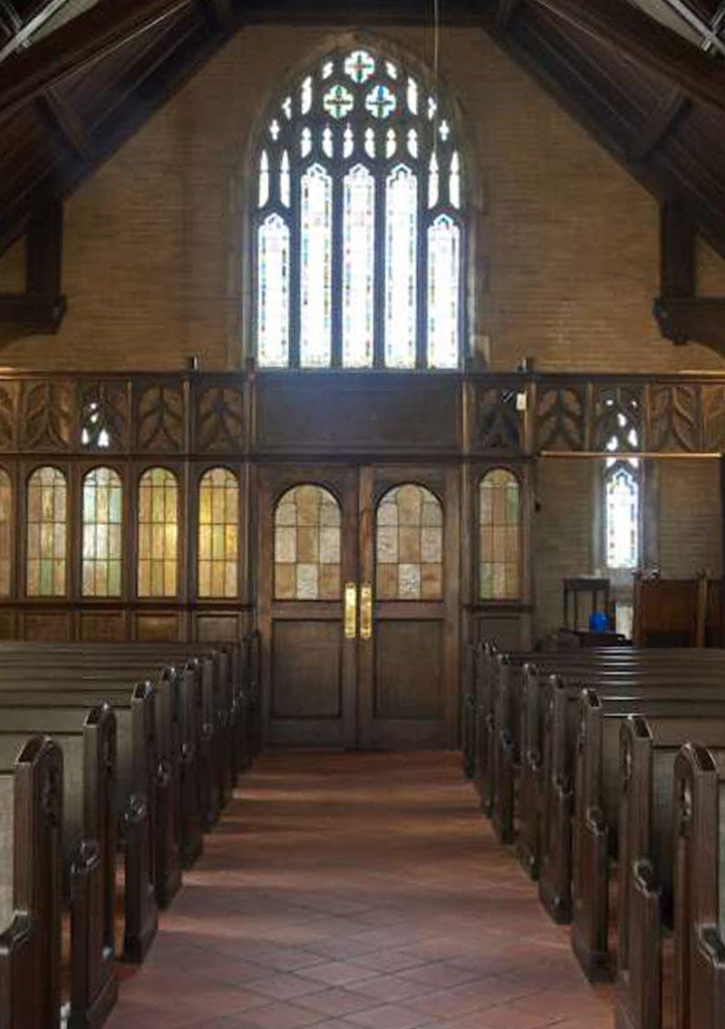 interior of chapel with large stained glass windows and the tiled center aisle lined with wooden pews