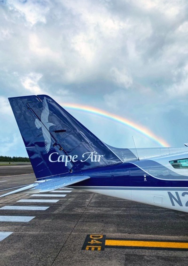 tail of small blue and white aircraft with rainbow in background