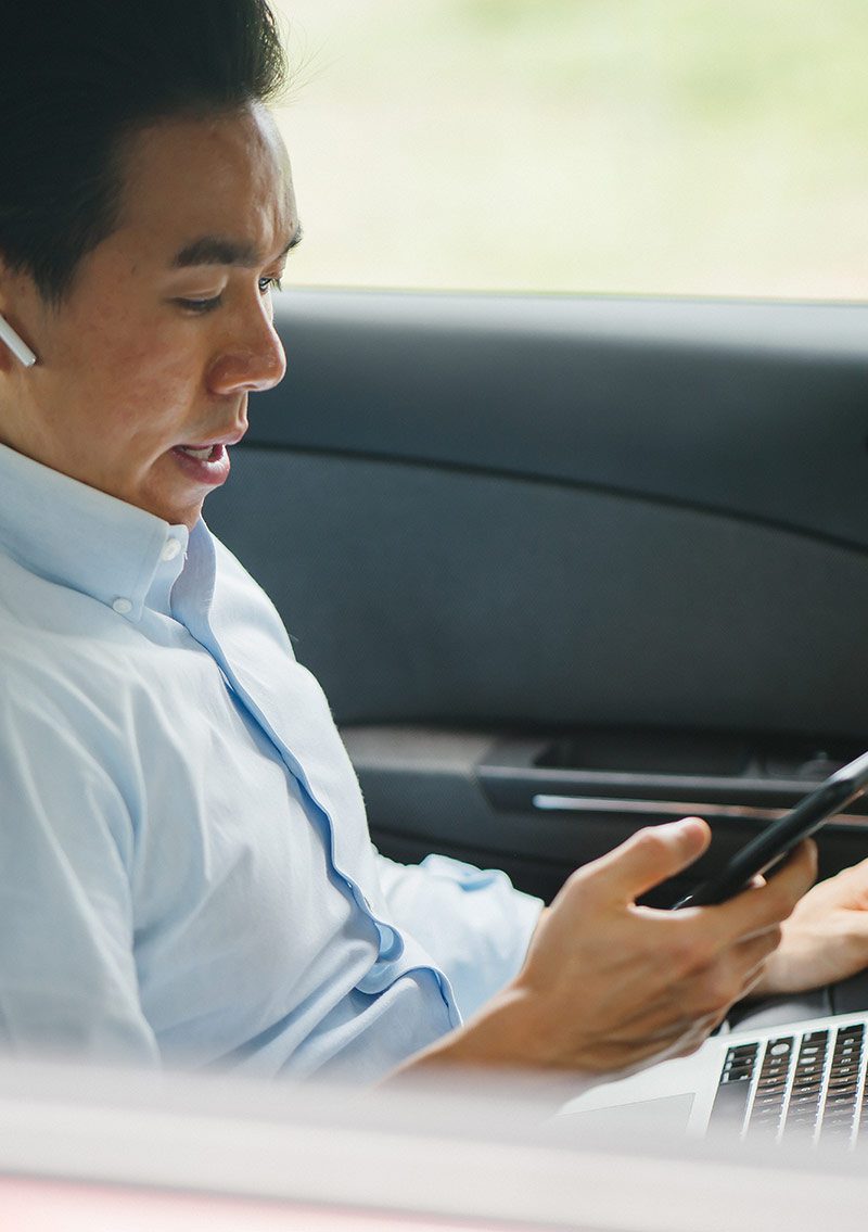 business person using devices in back seat of car